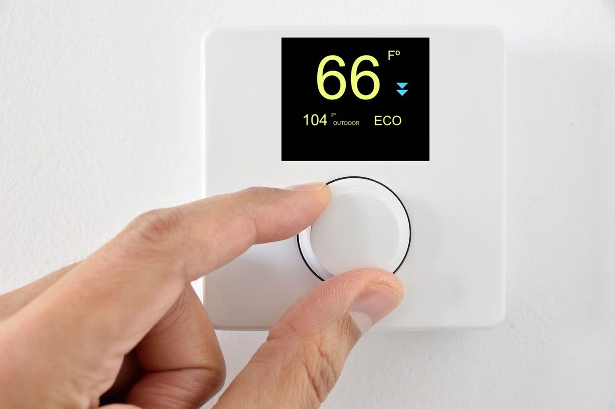 A person is adjusting the temperature on an electric thermostat.